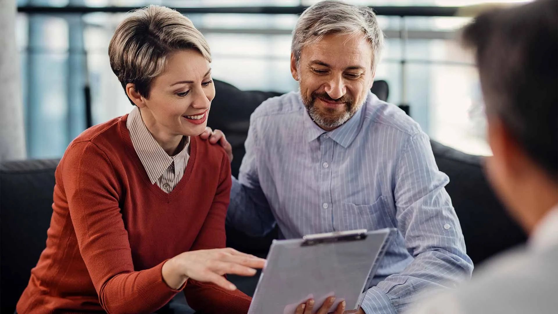 a man and a woman are sitting on a couch looking at a clipboard