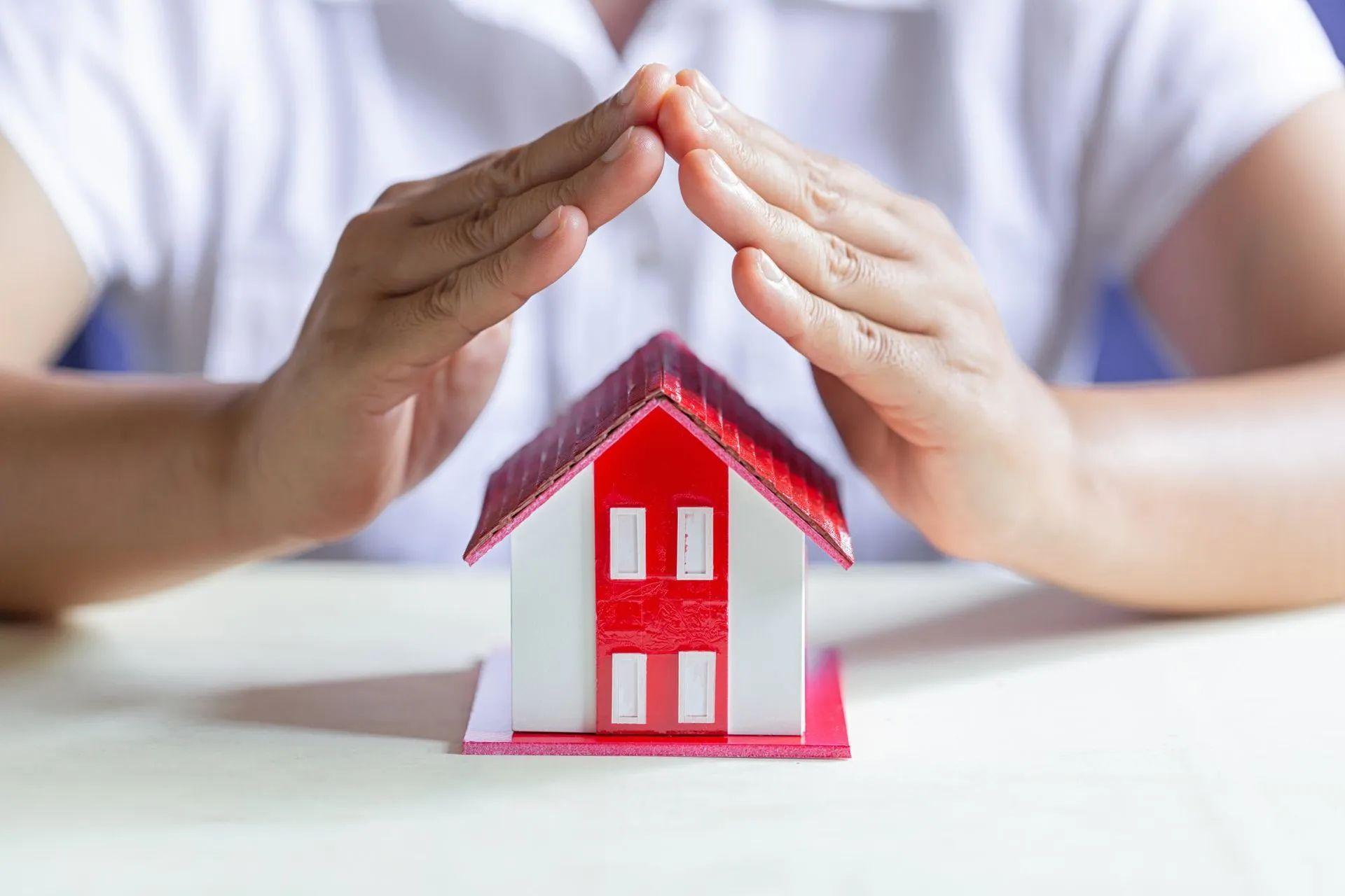 a person is covering a small red and white house with their hands