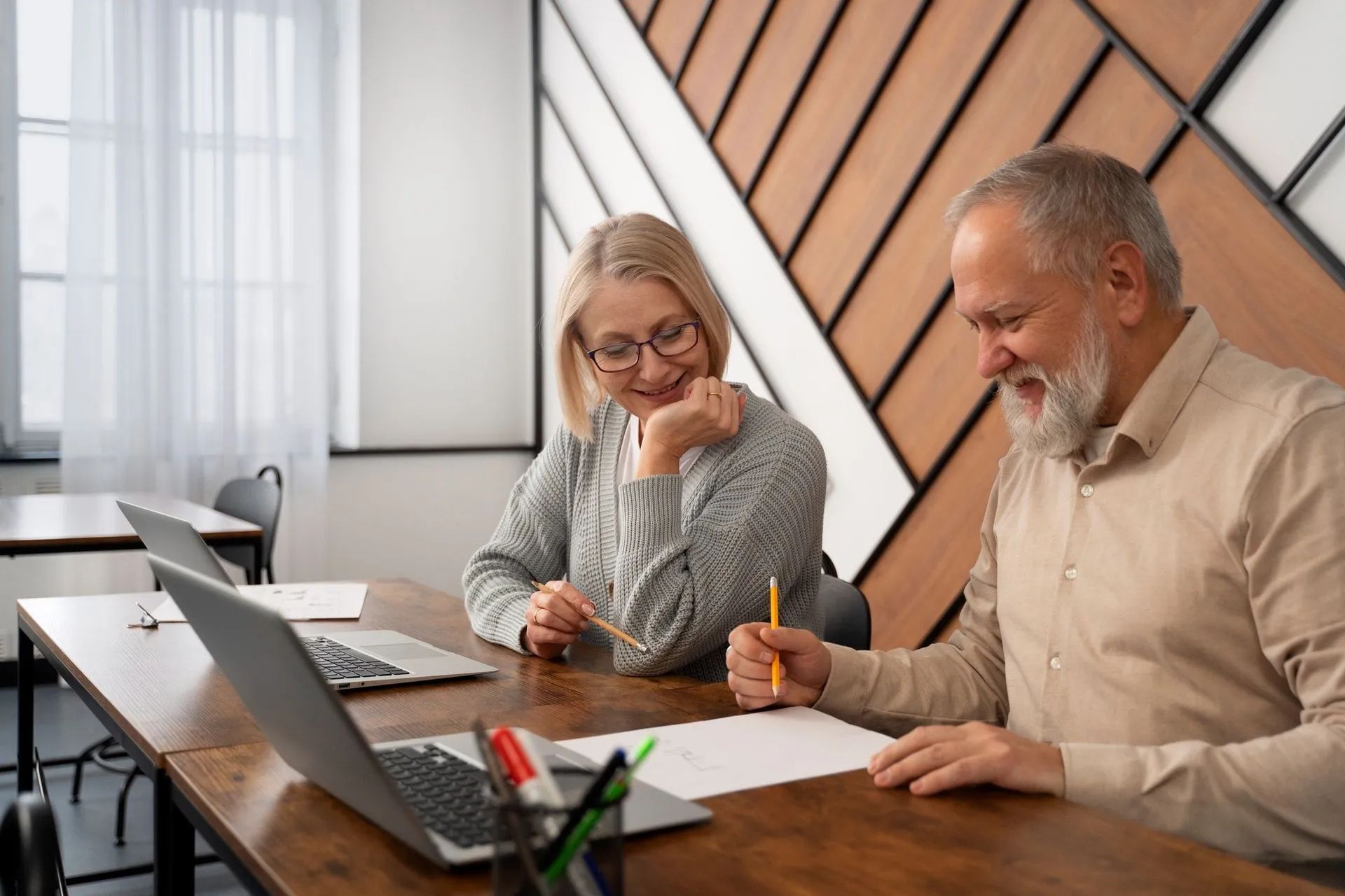 old man and woman are sitting at a table with laptops