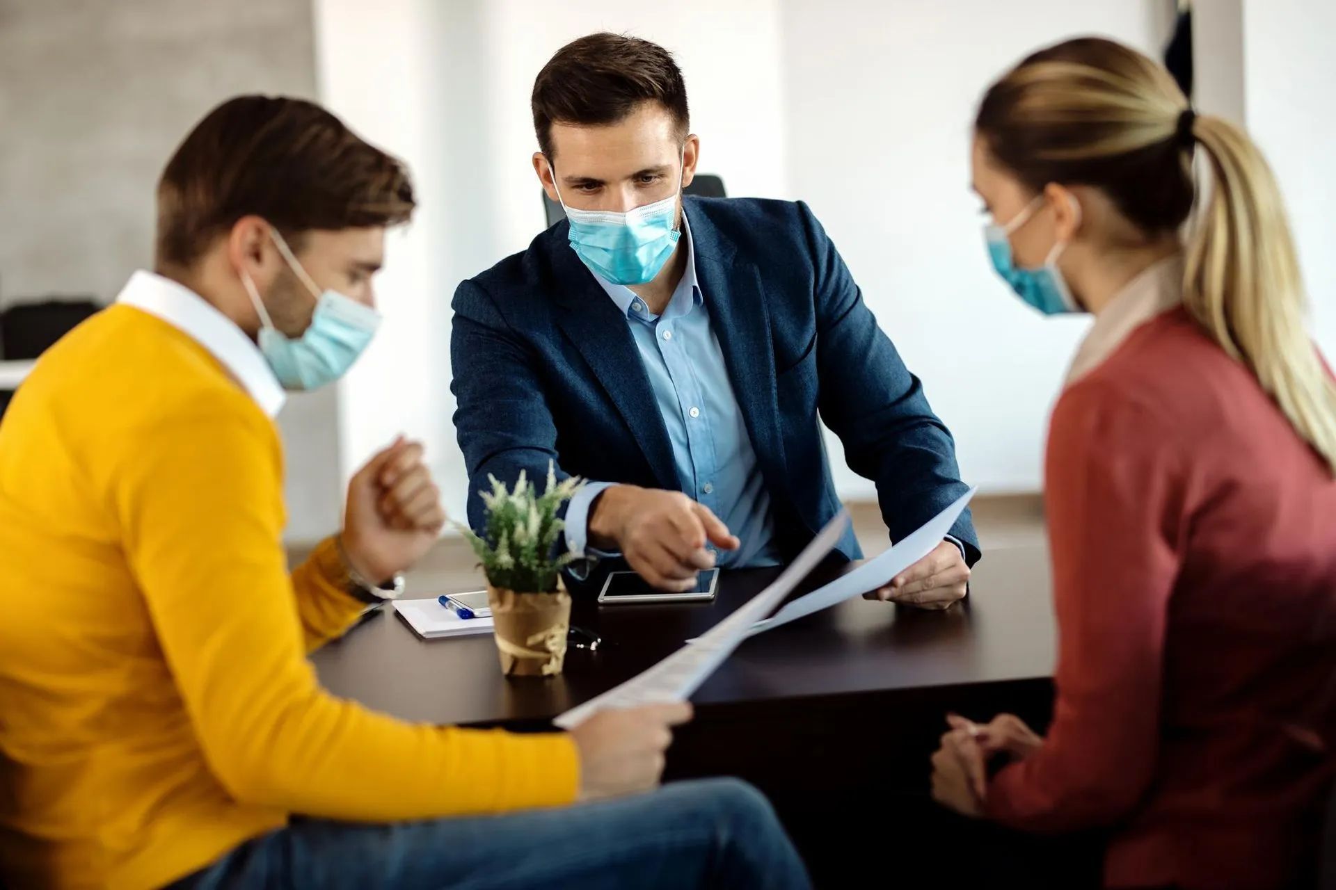 two men and a woman wearing face masks are sitting at a table