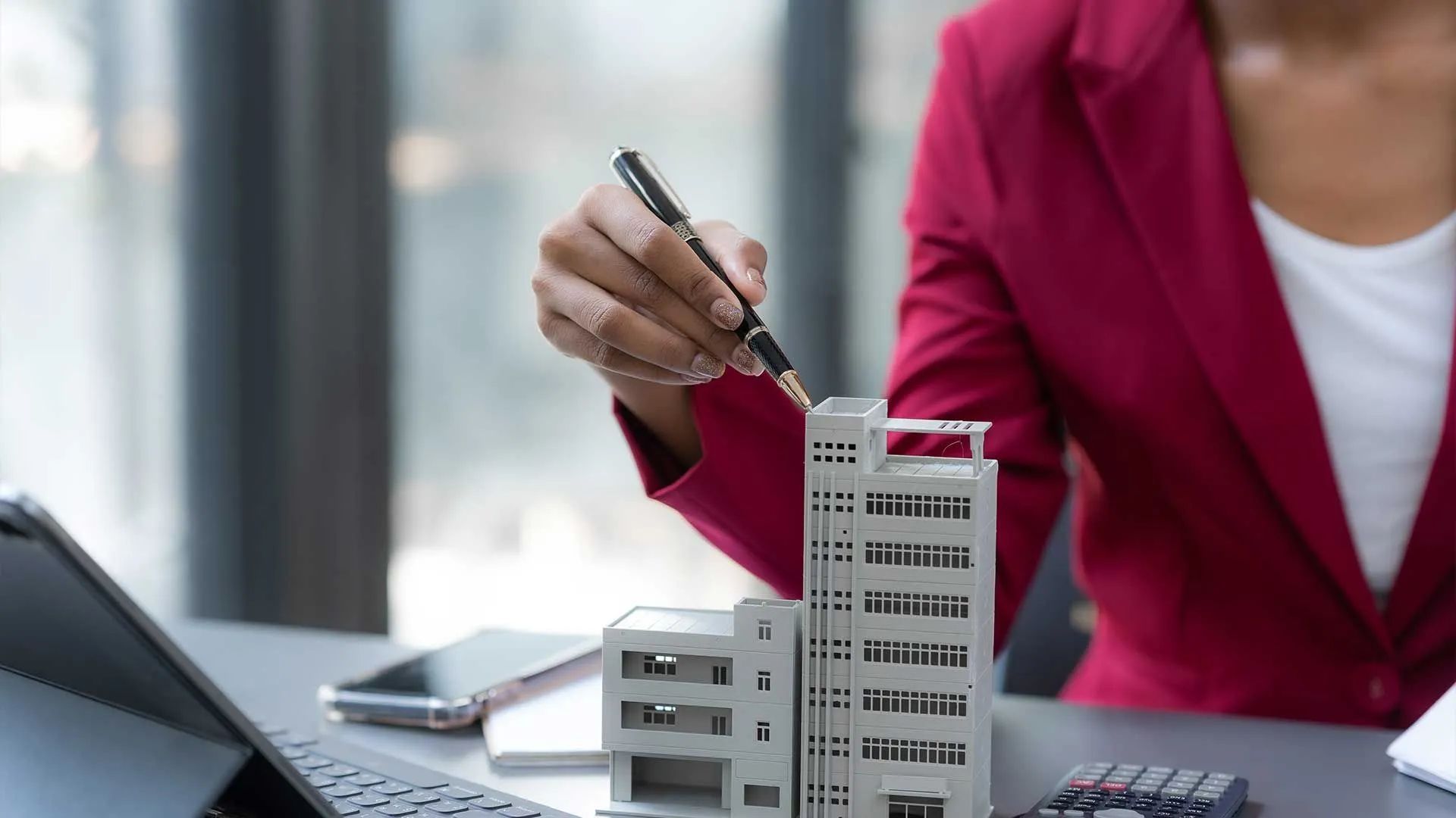 a woman is sitting at a desk holding a pen and a model of a building