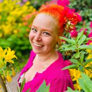 Eini Immonen from Rubylea Shop, with red hair is standing in front of a bunch of flowers.