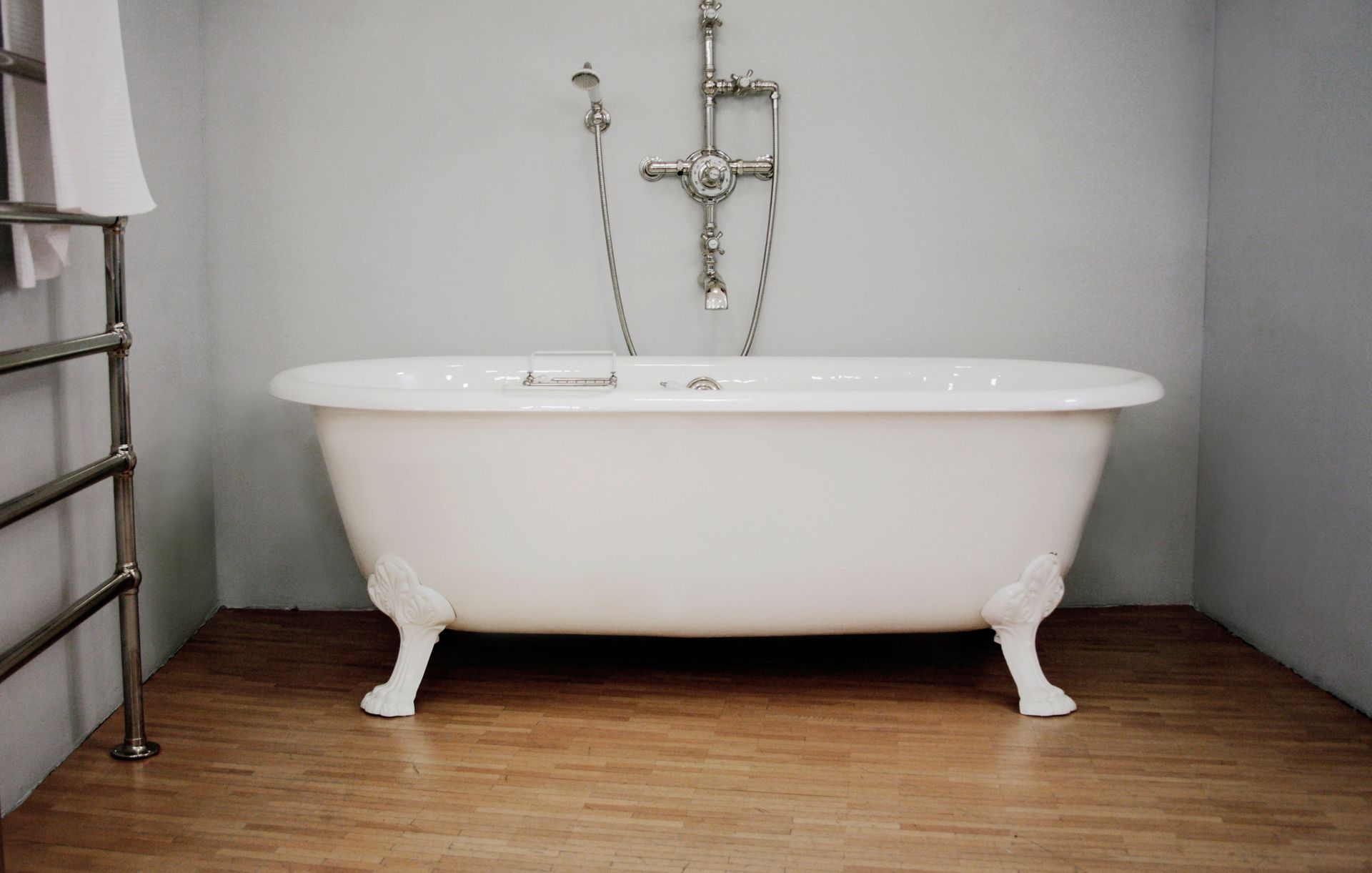 A white bathtub is sitting on a wooden floor in a bathroom.