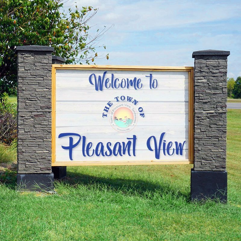 A welcome to pleasant view sign is sitting in the middle of a grassy field.