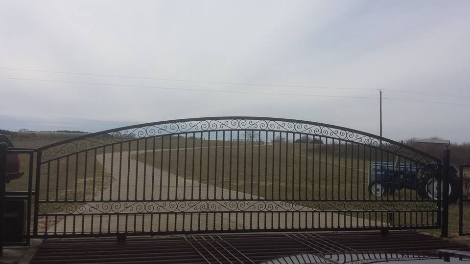 A large wrought iron gate is open to a dirt road.