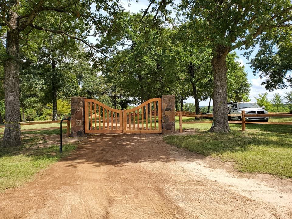 A wooden gate is sitting on the side of a dirt road surrounded by trees.