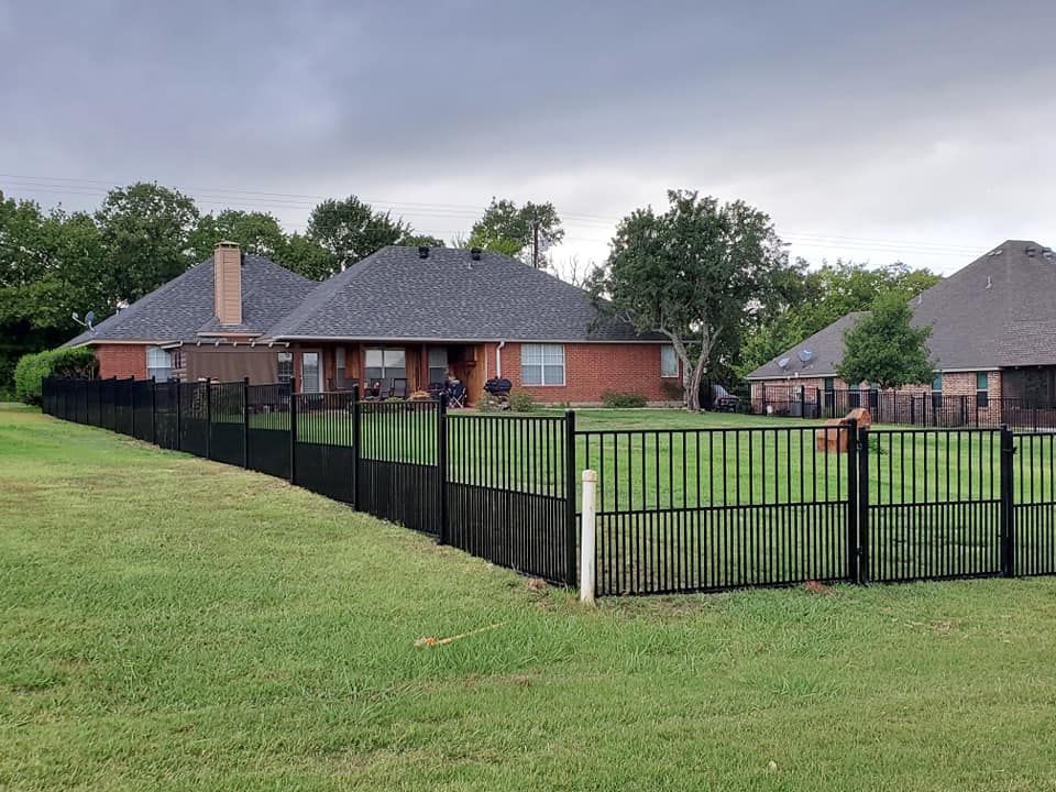 A black fence surrounds a lush green yard in front of a brick house.