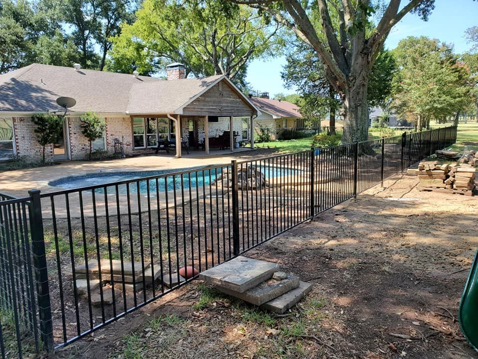 A wrought iron fence surrounds a swimming pool in front of a house.