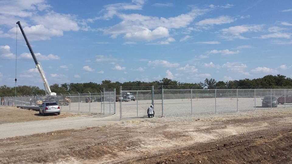 A crane is sitting in the middle of a dirt field next to a fence.