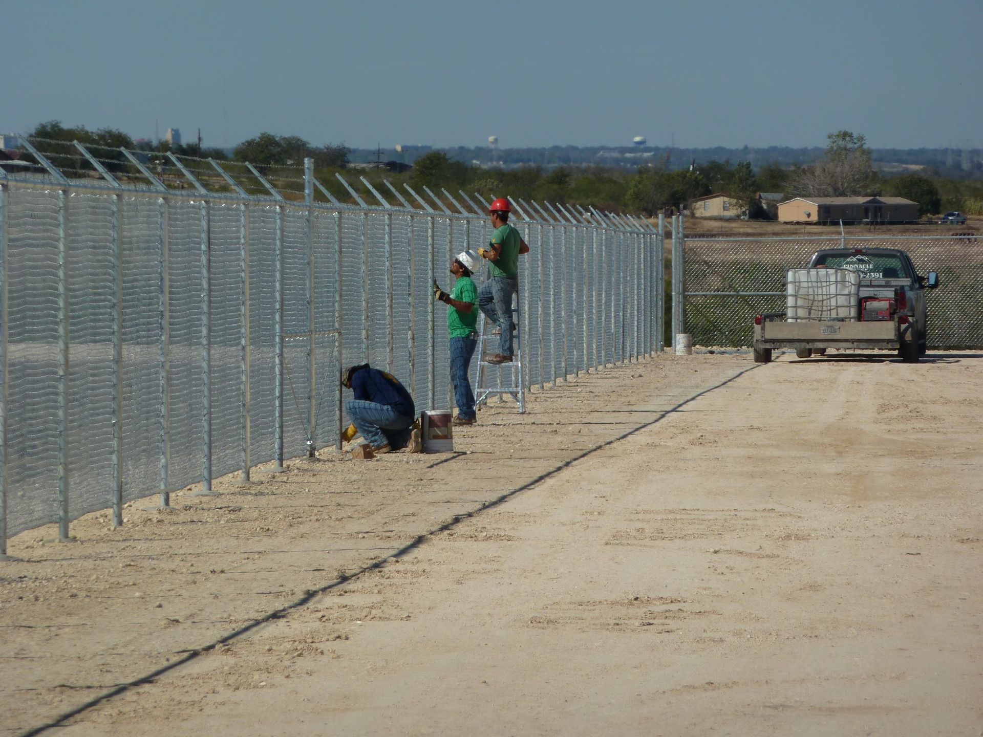 Two men are working on a fence with a truck in the background