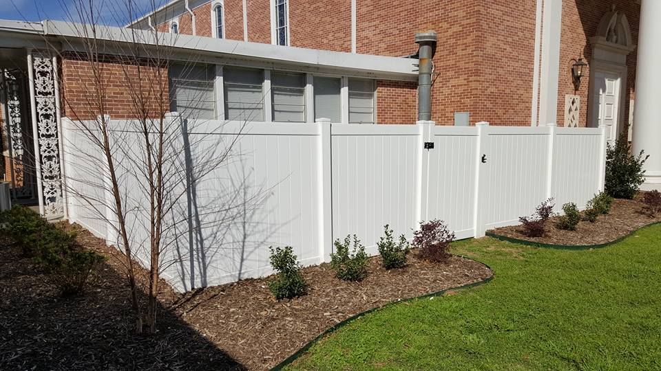 A white fence is in front of a brick house.