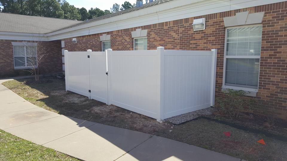 A white fence is sitting in front of a brick building.