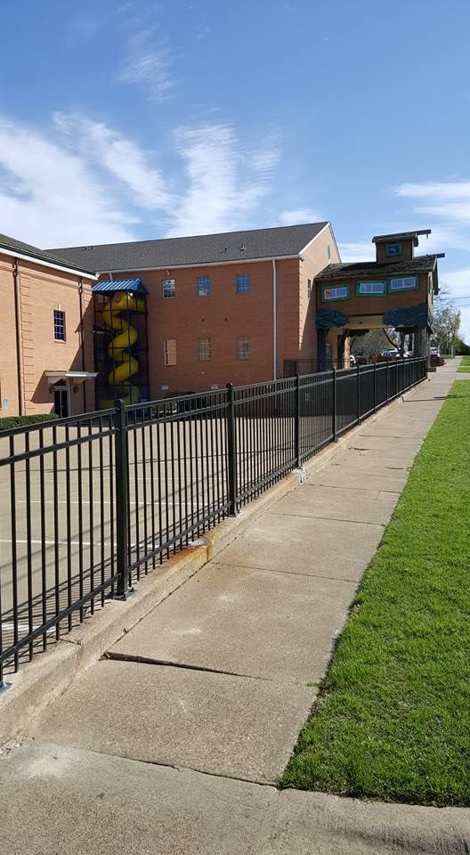 A fence surrounds a sidewalk in front of a large building.