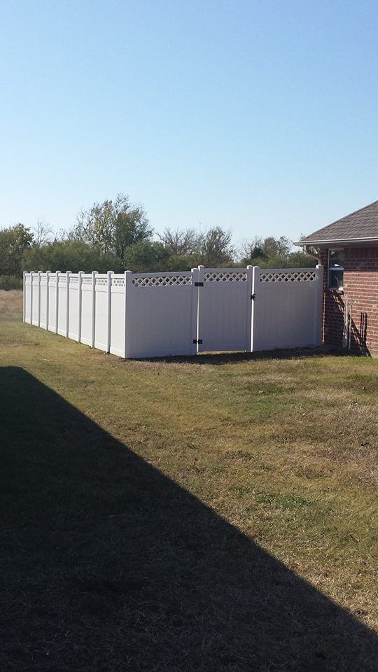 A white fence is in the middle of a grassy field next to a house.