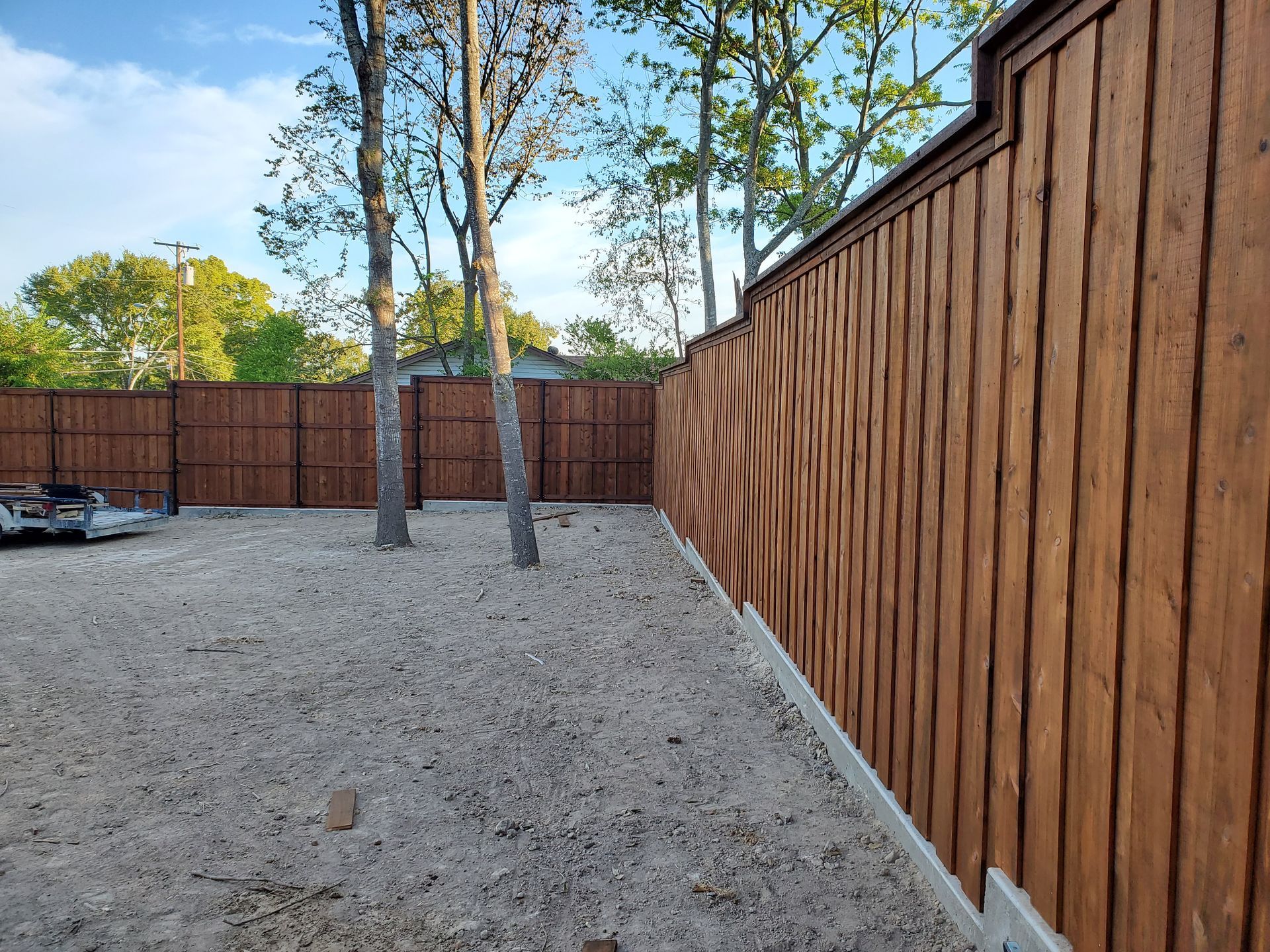 A wooden fence surrounds a gravel yard with trees in the background.