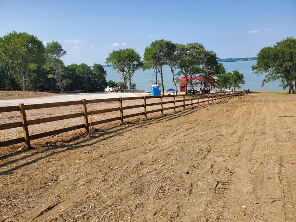 A wooden fence surrounds a dirt field with trees in the background