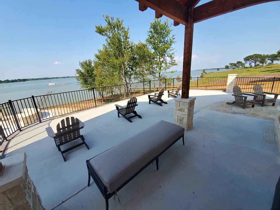 A patio with chairs and a bench overlooking a lake.