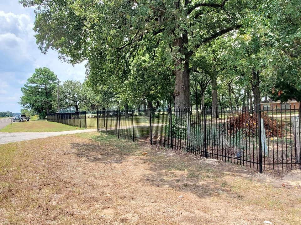 A metal fence surrounds a field with trees in the background.