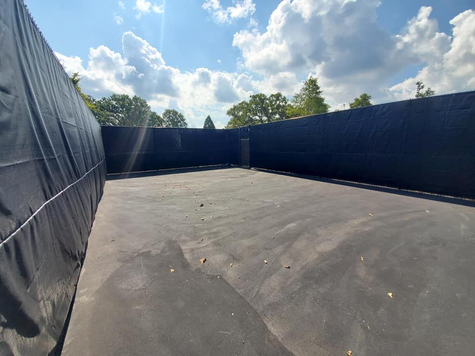 An empty tennis court with a blue fence and trees in the background.