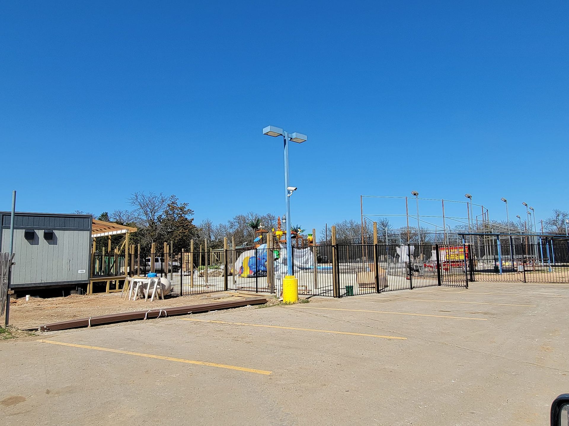 A parking lot with a fence and a playground in the background.