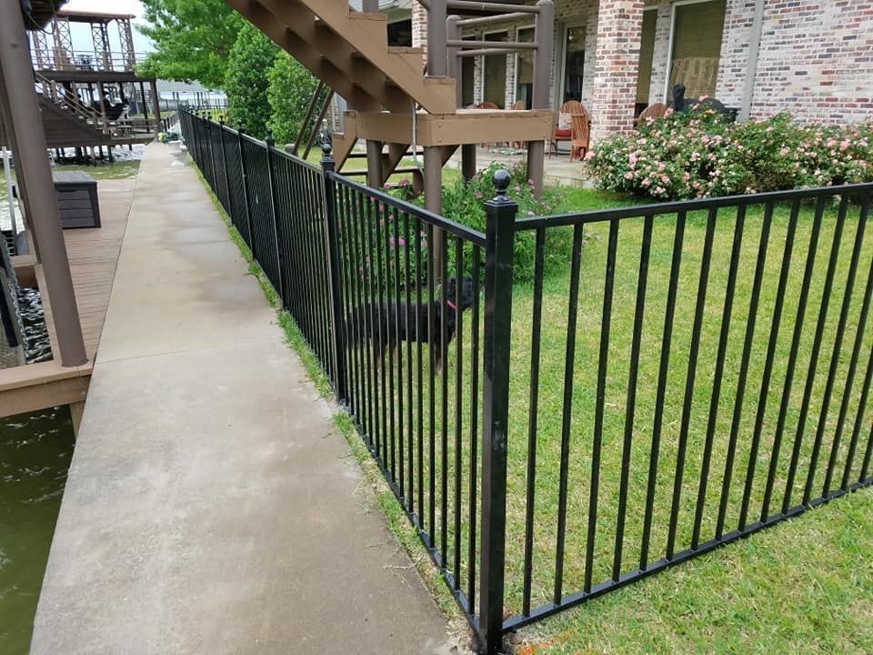 A black metal fence surrounds a lush green yard in front of a house.