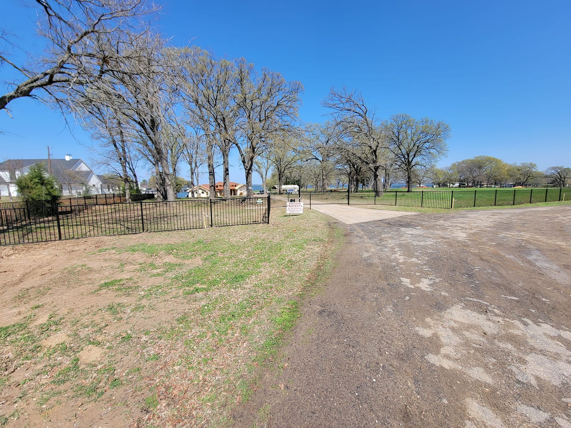 A dirt road going through a field with trees and a fence.