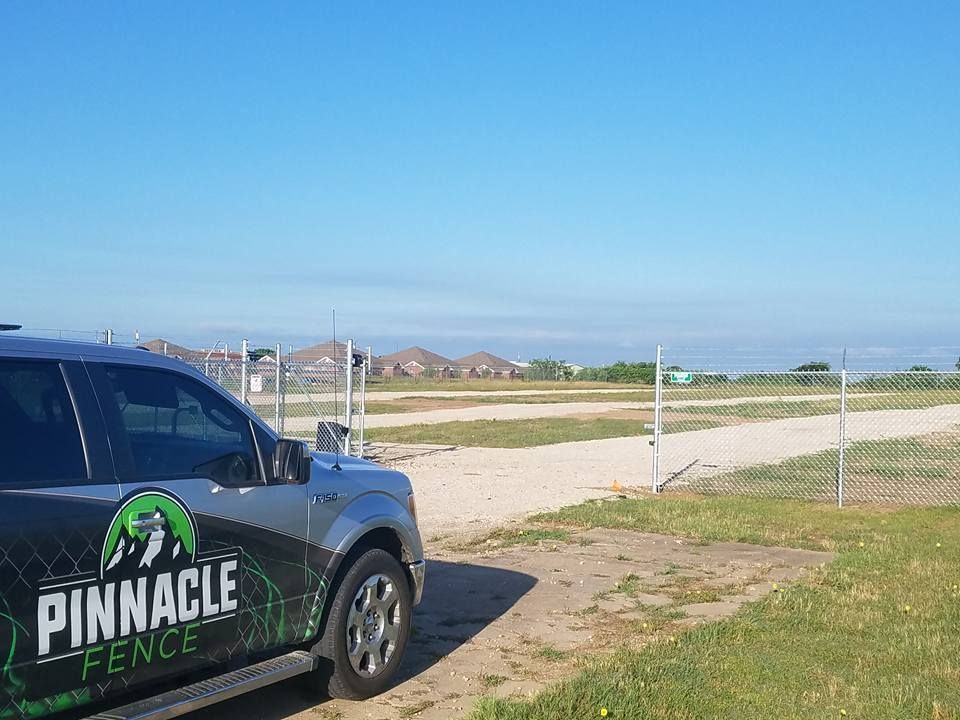 A pinnacle fence truck is parked in front of a chain link fence