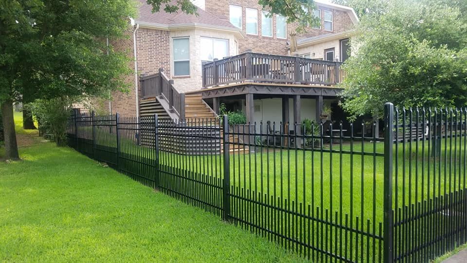 A black fence surrounds a lush green yard in front of a house with a deck.