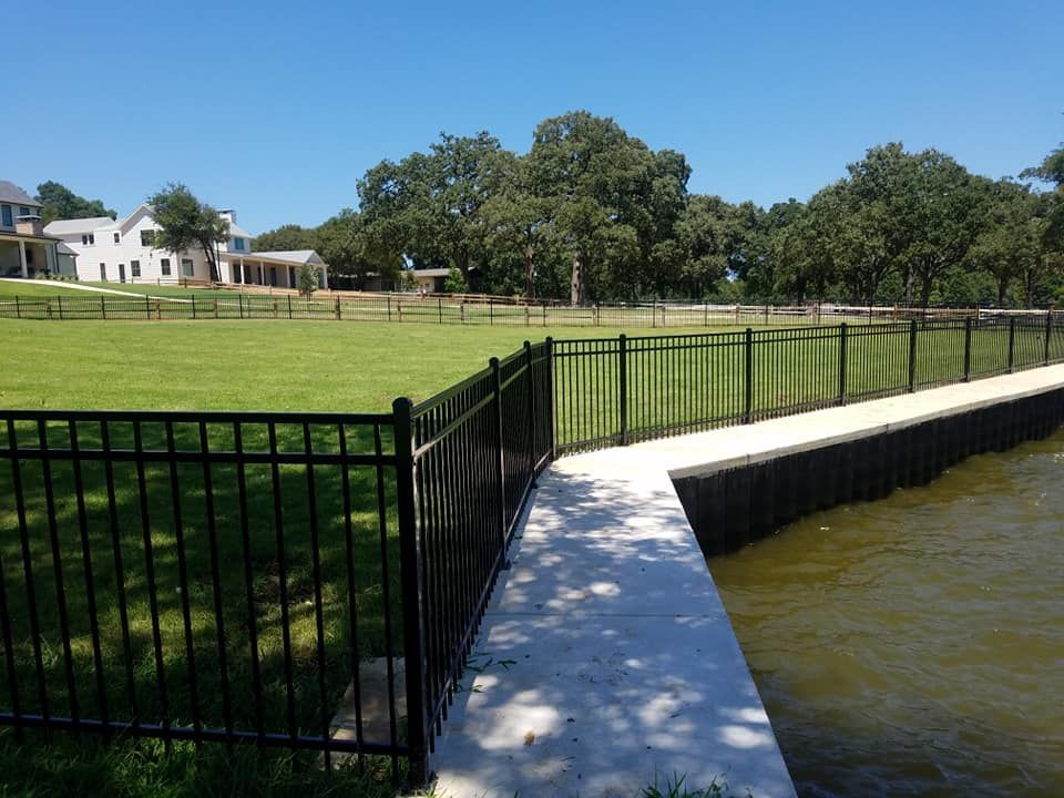 A fence surrounds a grassy field next to a body of water.