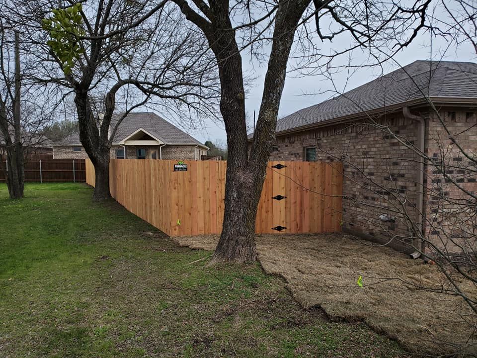 A wooden fence is surrounded by trees in front of a brick house.