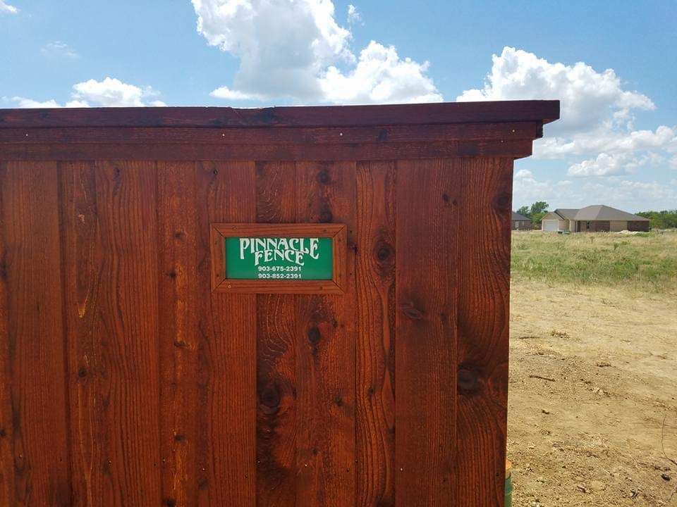 A wooden fence with a green sign that says pinnacle fence on it.