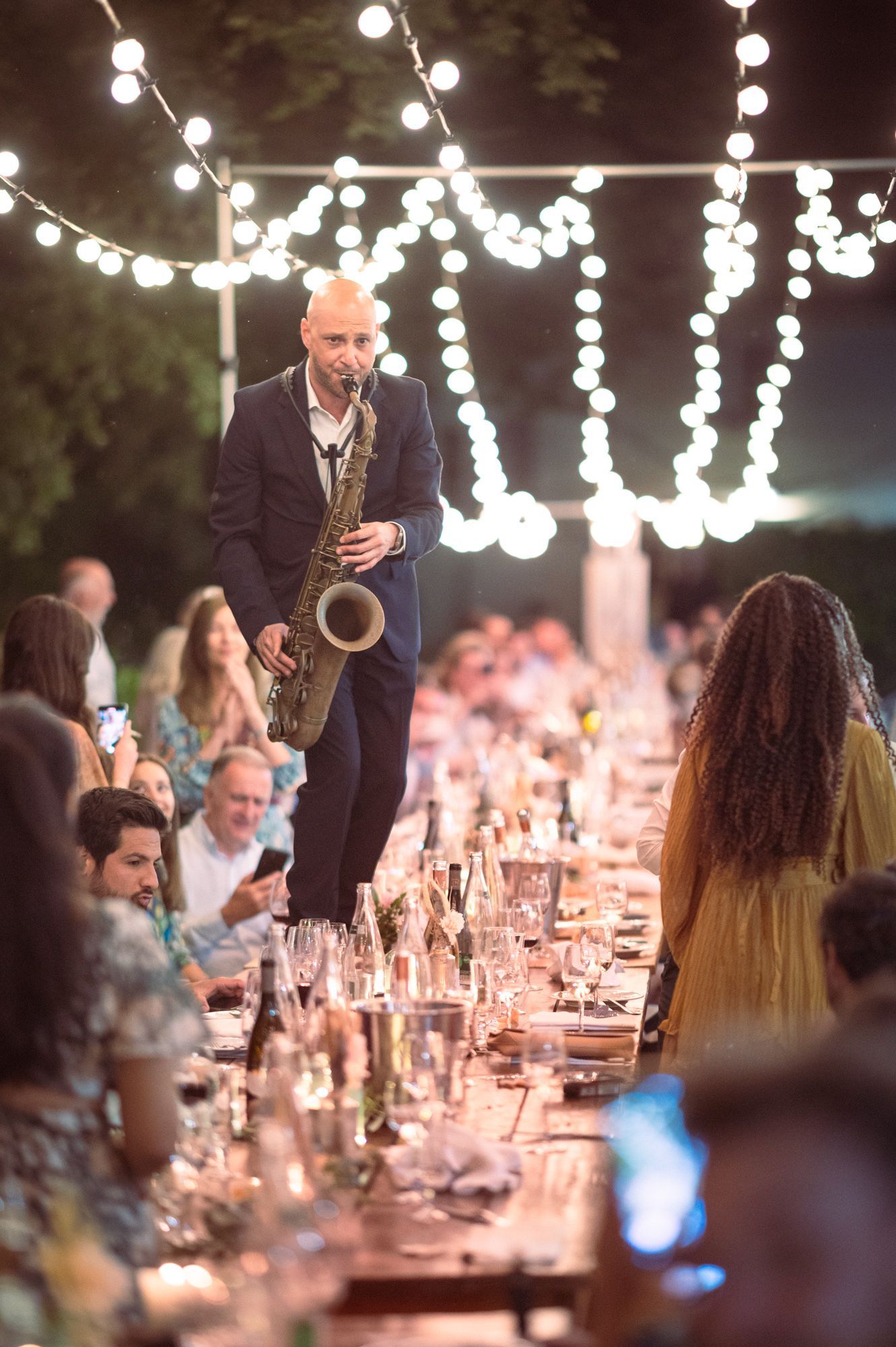 A saxophonist walks on tables as he plays at a luxury wedding reception in Provence.