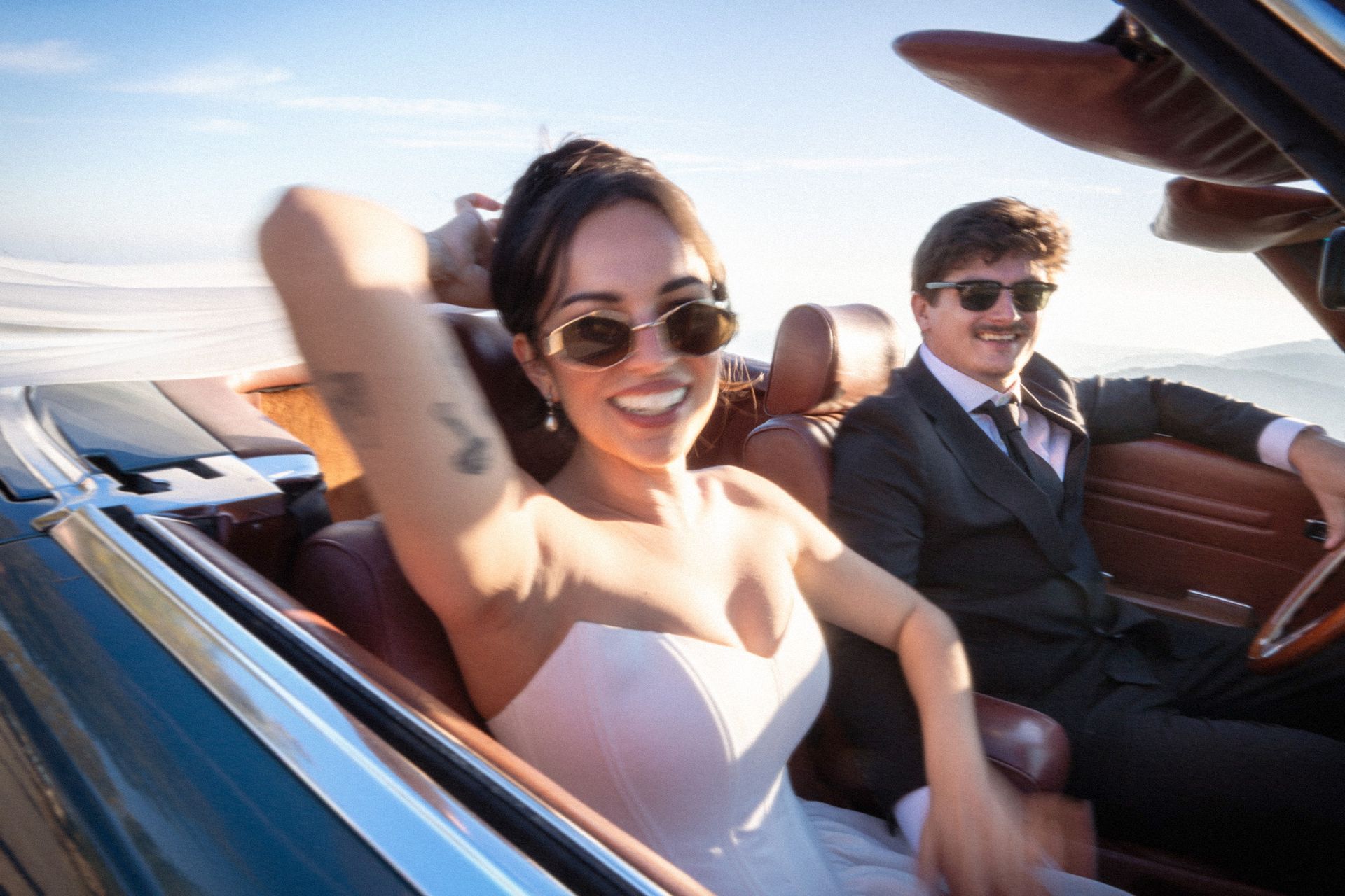 A bride and groom smiling in a open-top car during their elopement on he South of France.