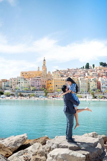 A couple embrace after a romantic proposal in Menton, French Riviera, with blue sky and sea.