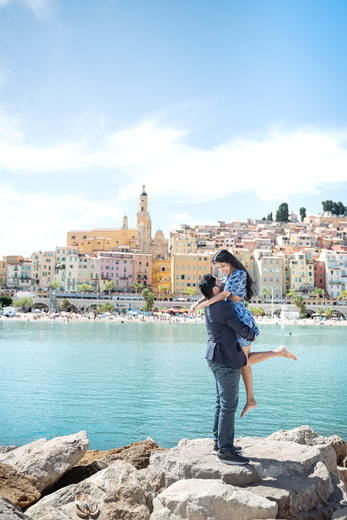 A couple embrace after a romantic proposal in Menton, French Riviera, with blue sky and sea.