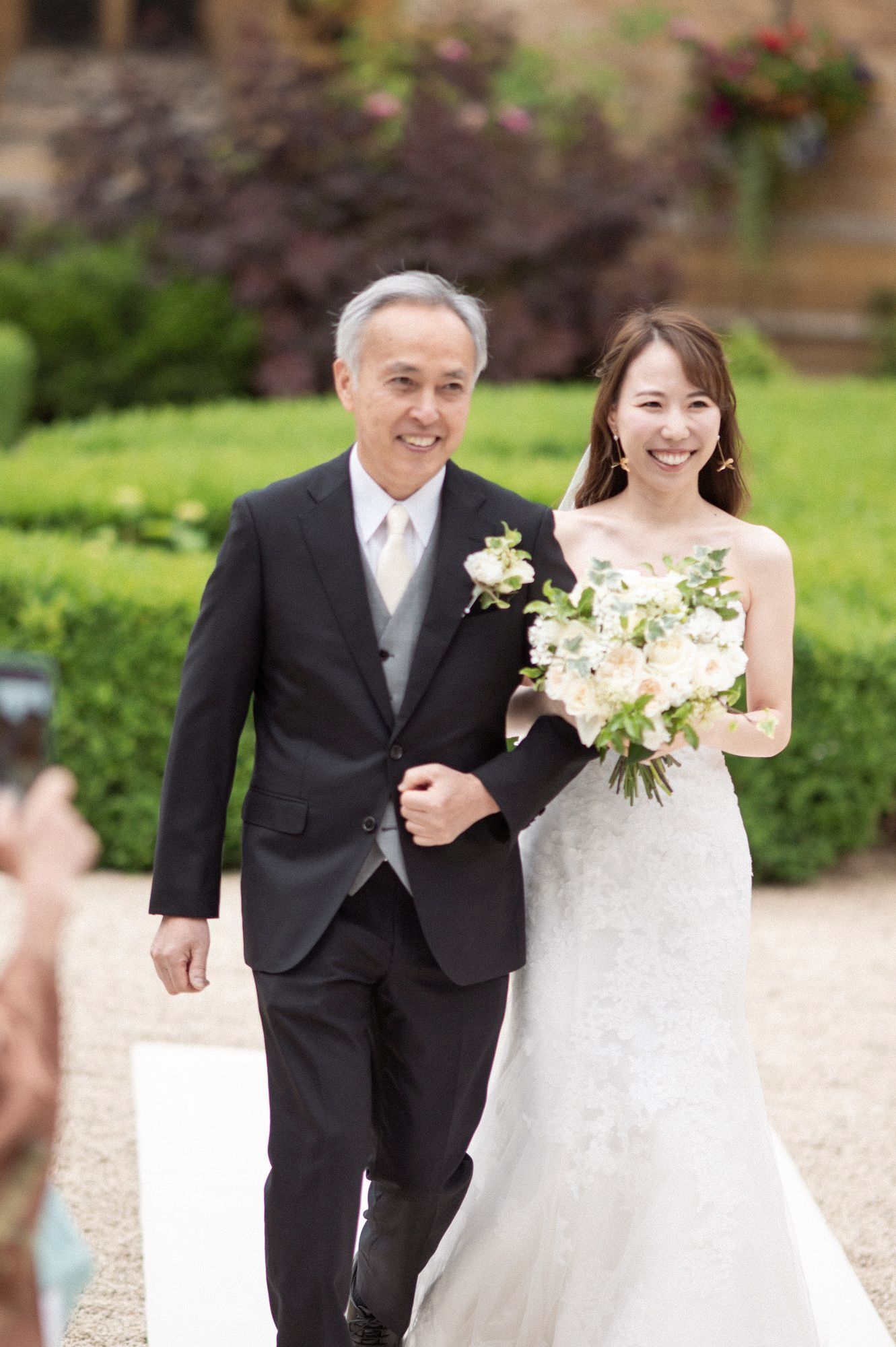 The bride walking down the aisle with her father at an outdoor ceremony at Ettington Park wedding venue