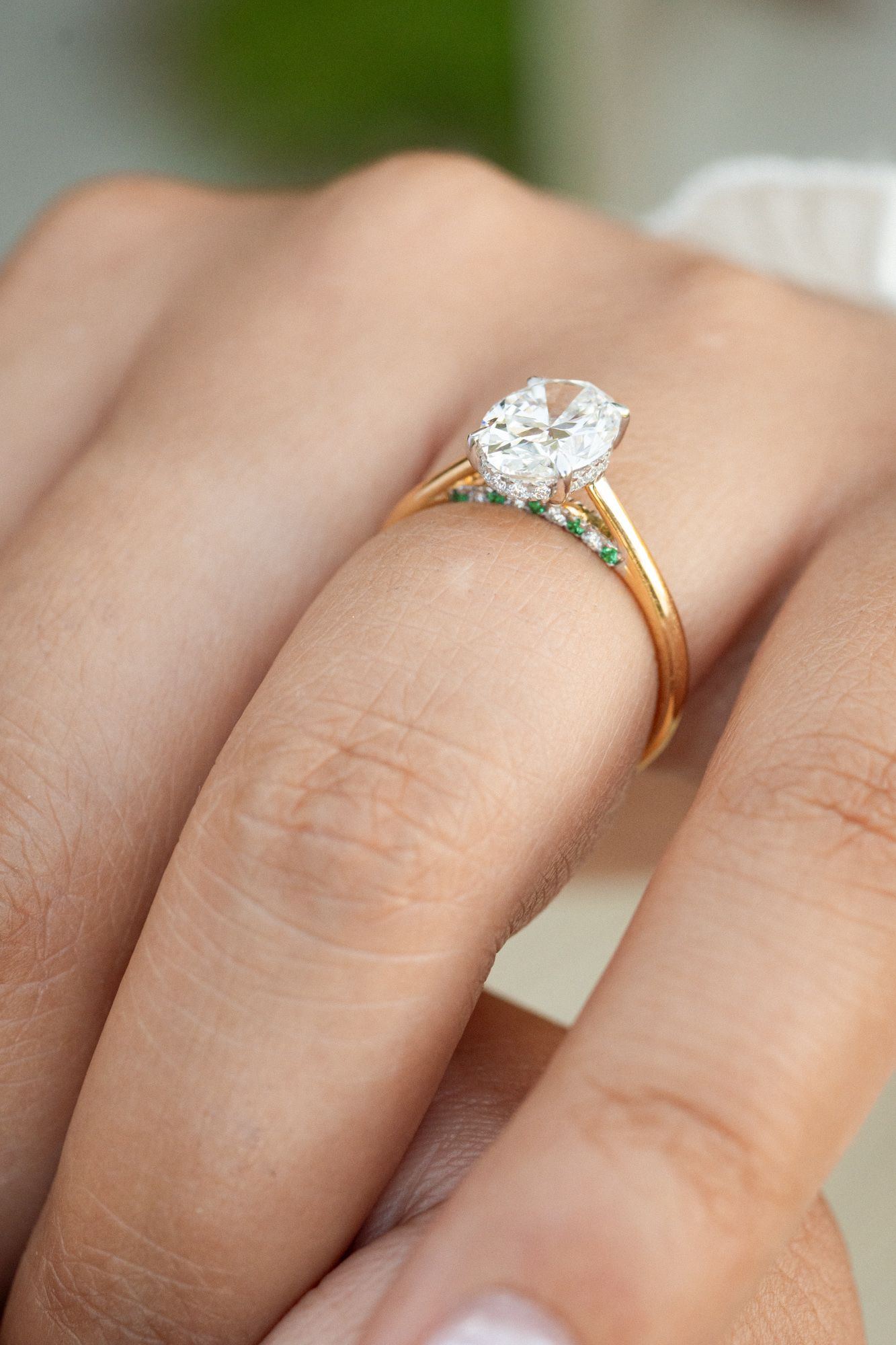 A close up of a diamond engagement ring encrusted with green emeralds.