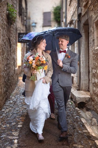 A bride and groom walking under an umbrella through St Paul de Vence in the rain on their wedding day.