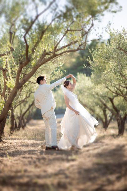 Un couple en tenue de mariage dansant dans une oliveraie à l'heure dorée au Château Font du Broc en Provence, France.