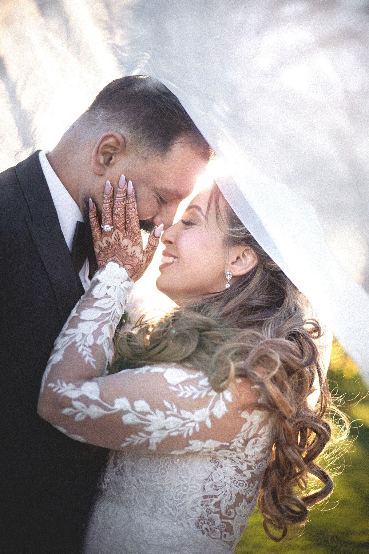 photo d'un couple sous le voile d'une robe de mariée contre-jour à l'heure dorée