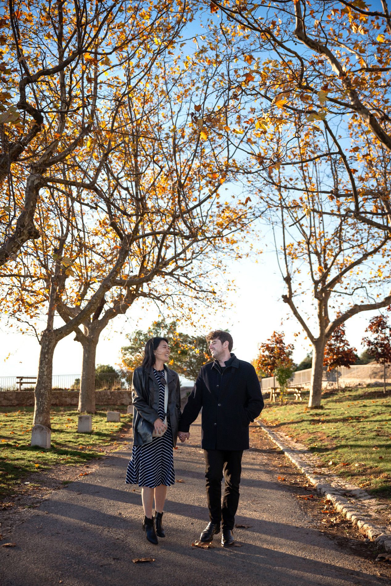 A couple laugh and smile as they walk during a candid photoshoot under autumn trees.