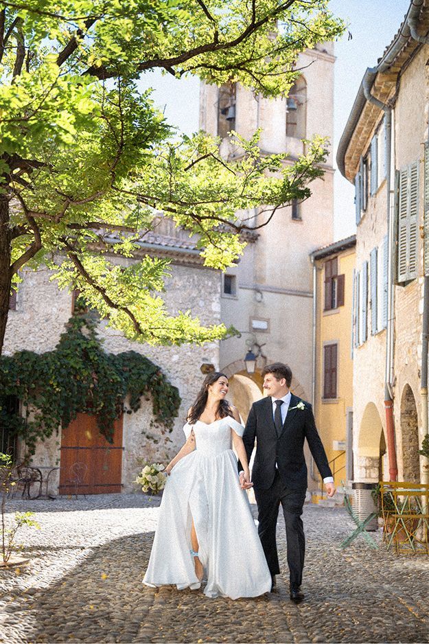 A couple on an elopement in the South of France laugh as they walk through the medieval streets of Cagnes sur Mer together during a photoshoot.