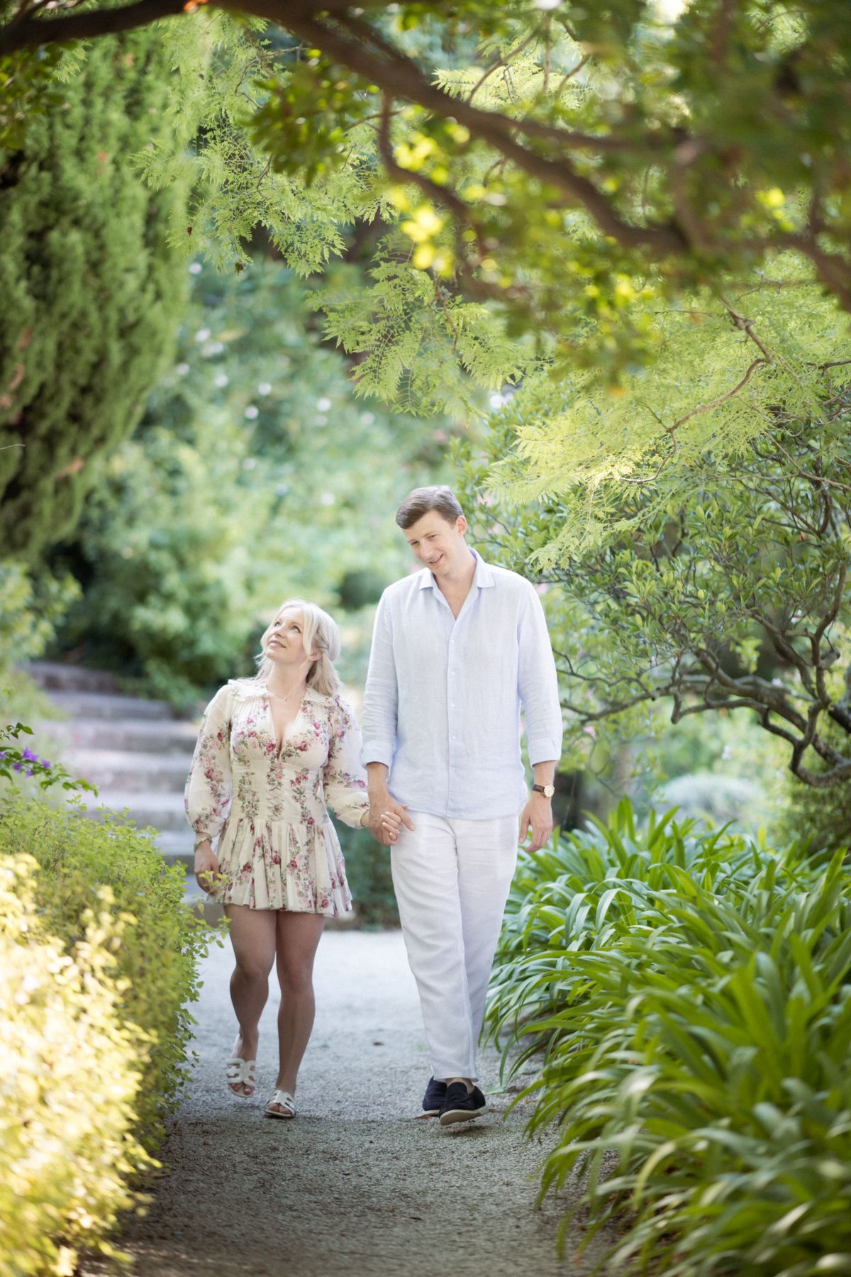 A couple laugh at they walk down a path at Villa Ephrussi after their engagement.