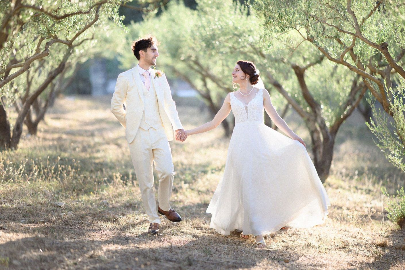 A bride and groom in Provence holding hands and laughing in an olive grove.