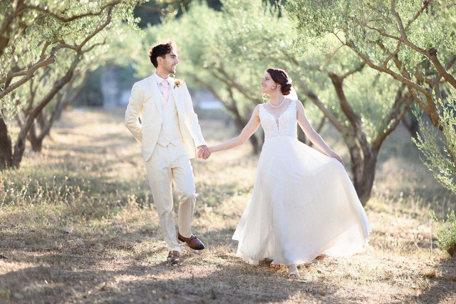 A bride and groom in Provence holding hands and laughing in an olive grove.