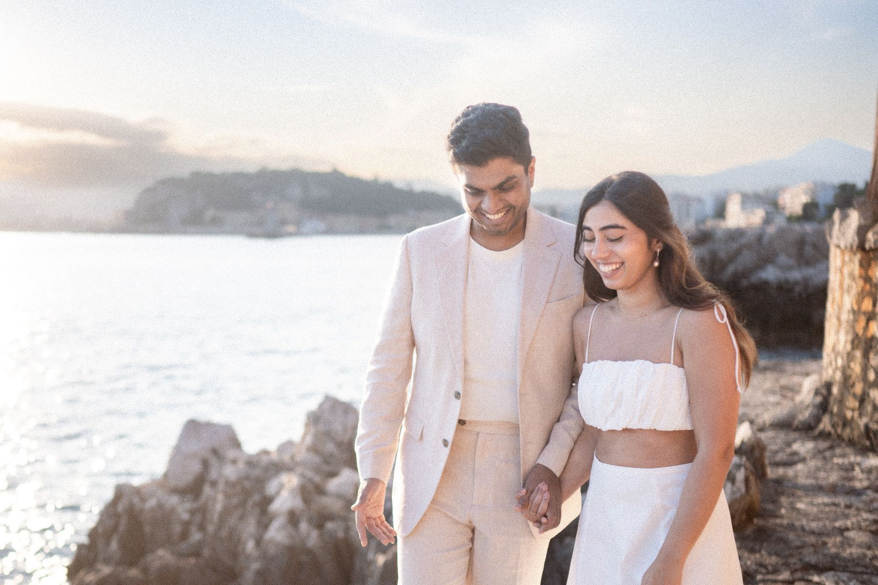 A couple laugh as they walk along a coastal path during the sunset.