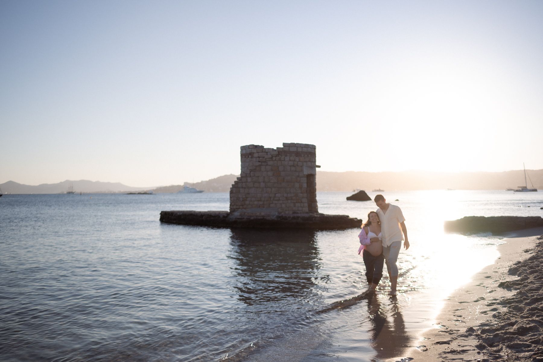 A couple walking on a sandy beach at sunset in Antibes during a maternity photoshoot.