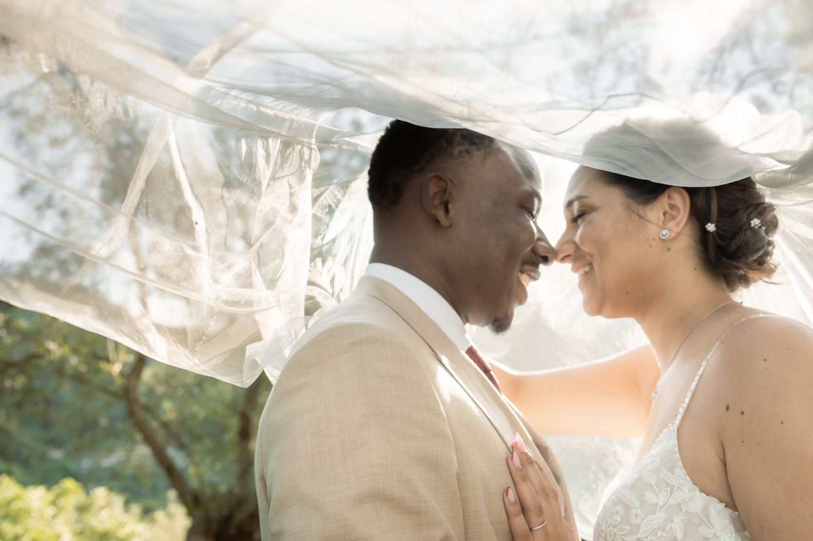 A backlit, romantic wedding photography image of a couple beneath the wedding dress veil.