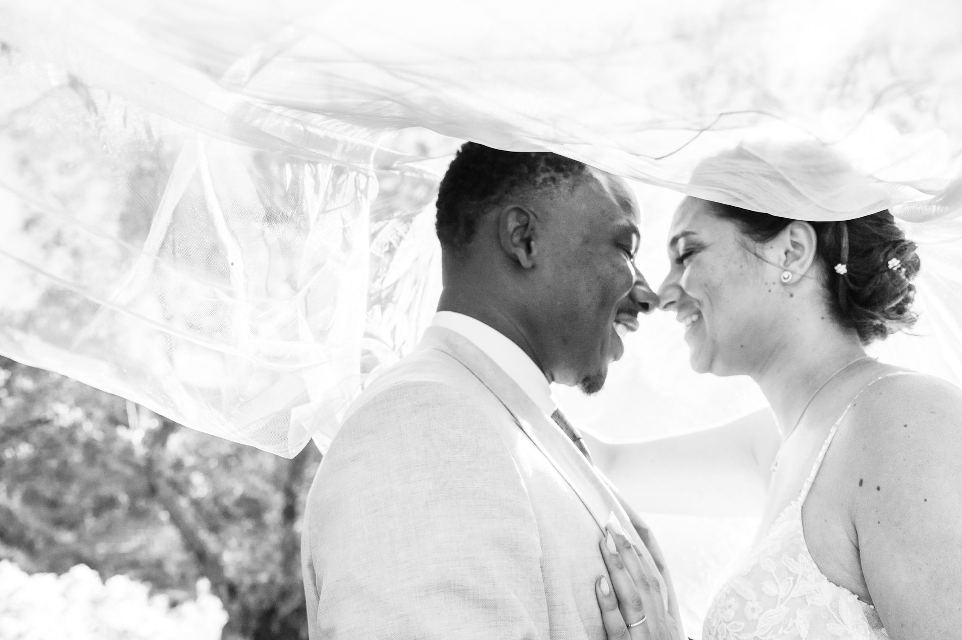 une photographie de mariage prise sous le voile de la mariée et à contre-jour, le couple est souriant