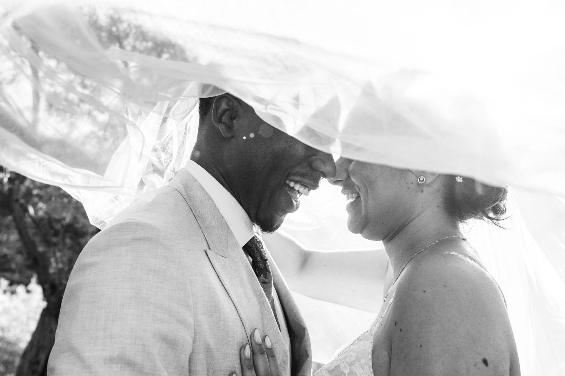 une photographie de mariage prise sous le voile de la mariée et à contre-jour, le couple est souriant